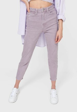 Woman wearing high-waist, light purple skinny jeans, white sneakers, cropped fuzzy lavender top, and a loose checkered shirt.