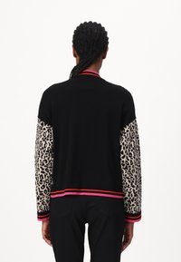 Schwarzer Cardigan mit Leopardenmuster-Ärmeln und rosa Akzentstreifen an den Bündchen und dem Saum. Strickstruktur, mittleres Gewicht, lässige Passform.