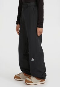 Zwarte waterdichte broek met een losse pasvorm, voorzien van een knoopsluiting in de taille en een driehoekig logo-opdruk op het onderbeen. Gladde textuur.