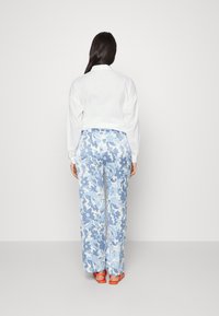 Camisa branca de manga longa combinada com calças largas de padrão floral em azul claro. O conjunto inclui sandálias laranjas com tiras.