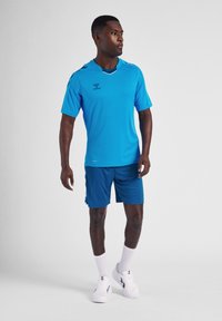 Blå atletisk t-shirt med korte ærmer og rund hals, parret med blå shorts. Accessories inkluderer hvide sokker og sorte atletiske sko.