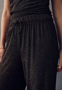 Černé, třpytivé joggingové kalhoty s elastickým pasem a šňůrkovým detailem; měkká textura s jemným leskem; volný střih.