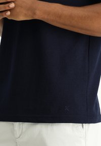 Granatowa bawełniana koszulka z krótkimi rękawami, z okrągłym dekoltem i małym logo blisko dolnego brzegu. Tkanina gładka.