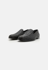 Black woven leather slip-on shoes with rounded toes, flat soles, and smooth texture, featuring intricate braiding detail on the upper.