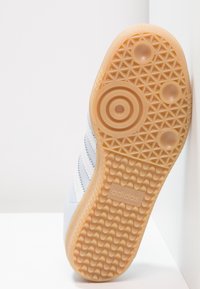 Bílá podrážka tenisky s texturovanou gumovou podrážkou, obsahující kruhový vzor a tři drážkované oblasti, na boku označená "adidas".