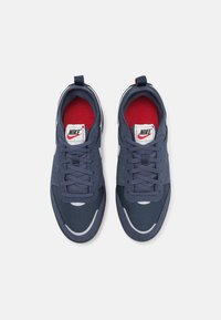 Nike sneakers with a navy mesh upper, red interior lining, white accents, and a textured finish. Features laces and padded tongue.