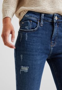 Tummansiniset farkut, joissa on kapea malli, antavat niissä käytetty vaikutelma ja repaleiset paikat. Kangas on sileä ja kestävä ompelu.