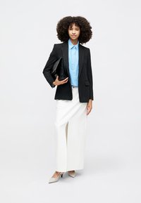 Black pinstriped blazer over a light blue button-up shirt, paired with a white maxi skirt featuring a side slit and beige high-heeled shoes.