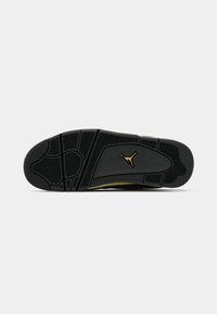 Semelle de basket noire avec des rainures à motifs et un logo Jumpman doré centré sur le dessous, présenté sur un fond blanc uni.