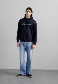 Felpa navy con testo grigio, abbinata a jeans svasati azzurri chiari e sneakers nere. Tessuto morbido e vestibilità rilassata in tutto.
