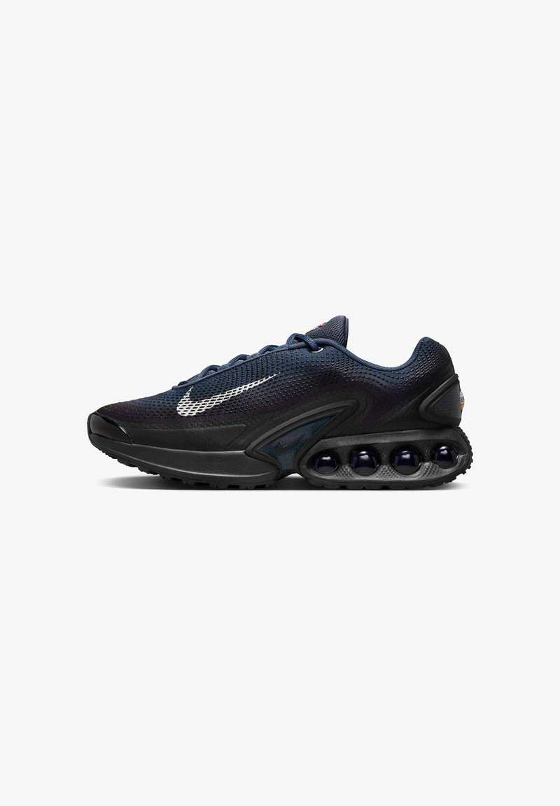 Scarpa sportiva nera con tomaia in mesh, accenti argentati e una suola arrotondata e audace con sfere scure per l'ammortizzazione. Design con lacci.