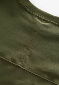 Maslinasto zelena pamučna majica s okruglim izrezom, koja ima ravne šavove i glatku, teksturiranu površinu tkanine.