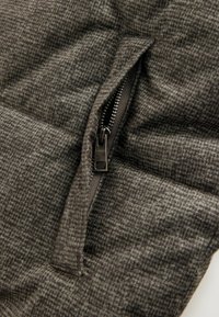 Tikkiliiniharmaa kangas, jossa on ruutukuosi, ja keskellä musta vetoketju, esittelee kohokohtia ja sauman yksityiskohtia.