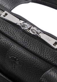 Sac à main en cuir noir avec surface texturée, fermeture éclair en métal argenté et détail logo distinctif. Forme rectangulaire compacte, design minimaliste.