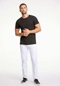 Schwarzes Baumwoll-T-Shirt kombiniert mit weißen Hosen und schwarzen Sneakern. Das T-Shirt hat einen Rundhalsausschnitt; die Hose hat ein enganliegendes Design.