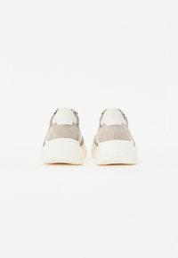 Sneakers med en kraftig hvit såle, overdel i grå semsket skinn og lær, og en glatt tekstur. Forsterket hæl og minimalistisk design uten synlig merkevare.