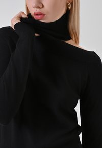 Maglione nero scollato sulle spalle con un design a collo alto a coste. Texture morbida con maniche aderenti, che mostrano un aspetto semplice e minimalista.