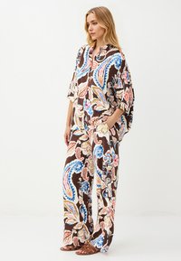 Braun gemustertes Outfit mit einem locker sitzenden Oberteil mit Kragen und weit geschnittenen Hosen, verziert mit floralen und Paisley-Designs in Blau und Pink.