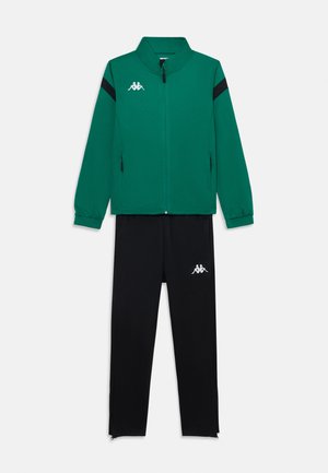 Zielona sportowa kurtka z zamkiem błyskawicznym, z czarnymi paskami i białym logo, w połączeniu z czarnymi spodniami dresowymi z białym logo i zamkami u kostek.