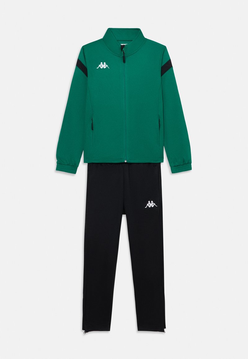 Groene sportjack met rits en zwarte strepen, vergezeld van zwarte joggingbroeken met een wit logo en ritssluitingen bij de enkels.