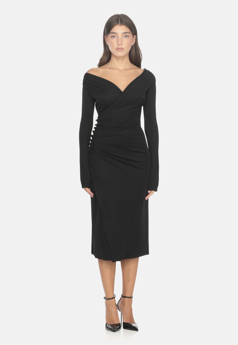 Abito nero a maniche lunghe, off-the-shoulder, con design avvolgente e dettagli arruffati laterali, realizzato in materiale elastico. Tacchi alti infuocati.