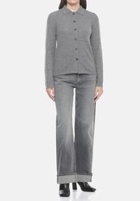 Cardigan in maglia grigia con scollo a collo, chiusura con bottoni e tasche frontali. Abbinato a jeans grigio chiaro a gamba larga e stivali neri con tacco.