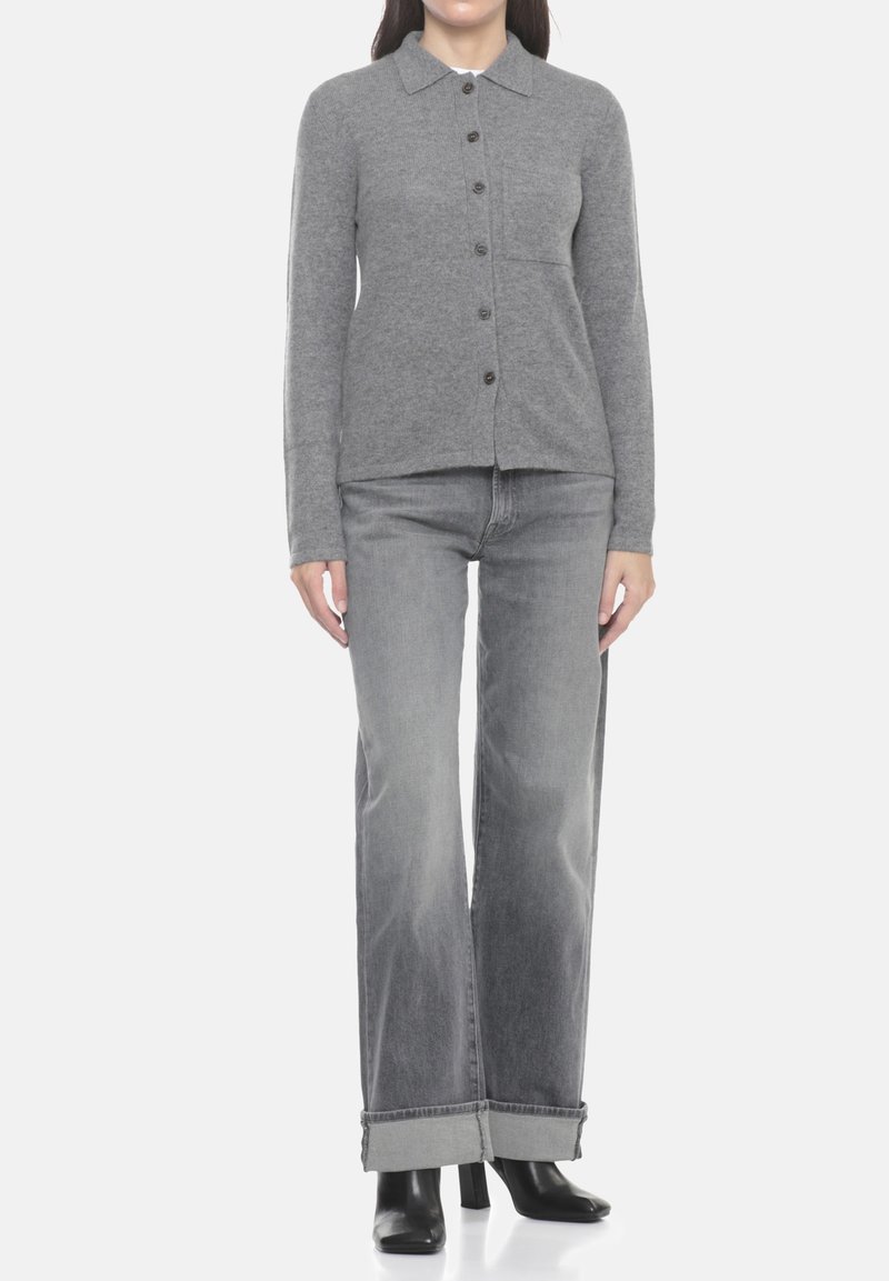 Cardigan in maglia grigia con scollo a collo, chiusura con bottoni e tasche frontali. Abbinato a jeans grigio chiaro a gamba larga e stivali neri con tacco.