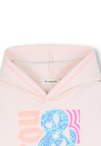 Haut à capuche rose clair avec une texture douce, présentant un design en sequins bleus scintillants en forme de "&" et des rayures roses d'accent sur la capuche. Étiquette : BILLIEBLUSH.