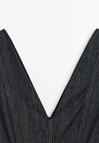 Tissu en denim foncé avec un col en V profond et des coutures jaunes visibles sur fond blanc.