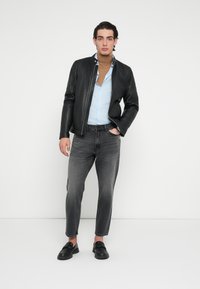 Czarna skórzana kurtka na jasnoniebieskiej koszuli, w zestawie z szarymi dżinsami i czarnymi wsuwanymi butami. Kurtka posiada zamek z przodu i dopasowany krój.