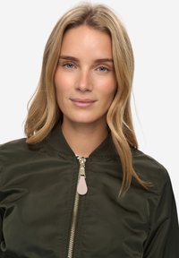 Olivově zelená bomber bunda s kovovým zipem, žebrovaným límcem a béžovým jezdcem na zipu. Hladký povrch, lehká látka, bez viditelných vzorů.