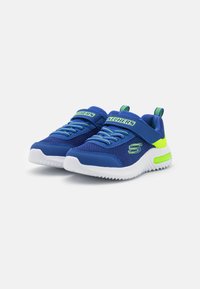 Baskets de sport en maille bleue avec une semelle en caoutchouc blanche, des accents verts, des lacets à l'avant et une sangle de maintien au milieu du pied.