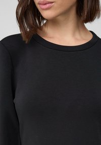 Czarna, długa bluzka z długim rękawem, z okrągłym dekoltem i gładką teksturą, z dopasowaną sylwetką wokół kołnierza i klatki piersiowej.