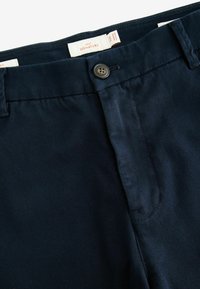 Pantaloni de culoare bleumarin, dintr-un material rezistent, având sistem de închidere cu buton în față, talie standard și o textură netedă cu cusături îngrijite.