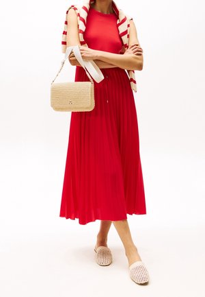 Robe plissée rouge avec un haut en maille texturée, sac à main en tissu beige tissé, et mules crème à bout ouvert. Stylisée avec un pull à rayures.
