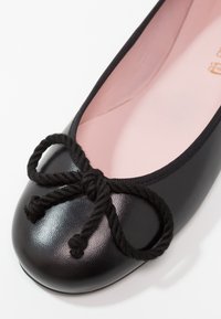 Ballerine noire avec surface texturée, bout arrondi, détail en nœud de corde noire et doublure intérieure rose clair.
