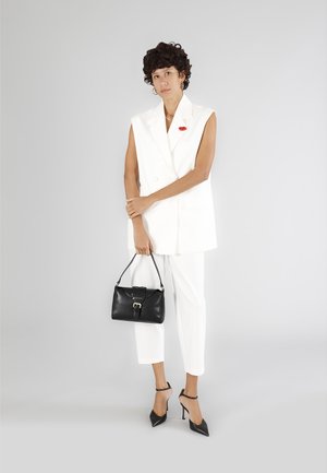 Hvid ærmeløs blazer og skræddersyede bukser parret med en sort taske og spidse højhælede sko. Har en rød accessory på blazeren.