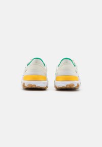 Light-colored sneakers with a textured fabric upper, green accents, and a yellow heel. White midsole with a patterned rubber outsole.
