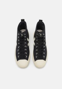 Czarne trampki typu high-top z płóciennym materiałem, białym gumowym noskiem, klasycznym sznurowaniem i charakterystycznym logo na języku.