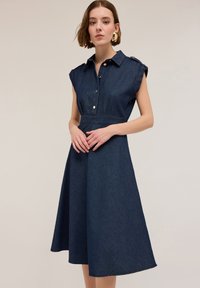 Denimmekko, jossa on lyhyet kääretakit, kaulus ja etupainikkeet. A-linjainen muoto, tumma sininen, sileäpintainen ja polvimittainen helma.