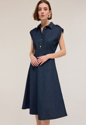 Rochie din denim cu mâneci scurte rulou, guler și nasturi pe față. Formă în A, de culoare albastru închis, cu o textură netedă și tiv până la genunchi.