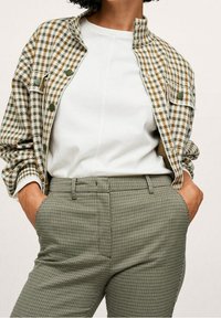 Veste à motif pied-de-poule avec des tons verts et marron, dotée de boutons-pression. Haut blanc et pantalon à carreaux cintré dans des tons verts.