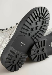 Bottines argentées à texture craquelée, avec une semelle en caoutchouc noir dotée d'un motif de semelle profond. L'étiquette indique "NEXT" et la taille "12."