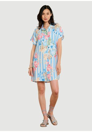 Frau trägt ein kurzärmeliges, knöpfbares Kleid mit blau-weißen Streifen und pink-blau-beigem Blumenmuster, kombiniert mit Riemchensandalen.