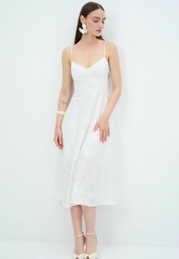 Witte jurk met bloemenborduursel, V-hals en dunne spaghettibandjes; midi-lengte, A-lijn silhouet, gestyled met bijpassende hakken en accessoires.