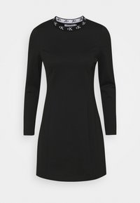 Svart långärmad klänning med hög krage som har en vit märkeskrage. Slät tyg med rak silhuett och smal passform.