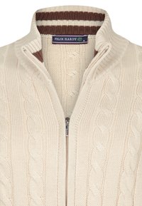 Suéter de lana crema de punto trenzado con cremallera y cuello alto, con ribetes a rayas en marrón y blanco. Presenta una cremallera de metal y una etiqueta de la marca.
