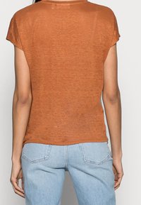 Rostfärgad kortärmad topp med avslappnad passform och mjukt, texturerat tyg. Avslappnad nederkant, bärs med ljusblå jeans.