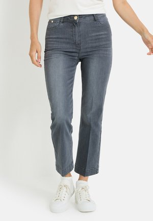 Jean en denim gris foncé, à coupe slim, jambes légèrement fuselées, avec fermeture à bouton. Associé à des baskets blanches.
