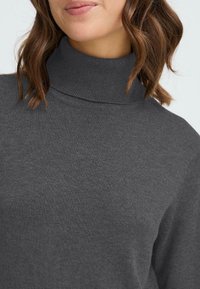 Mörkgrå turtleneck-tröja med ribbad halsringning. Mjuk tygetextur, med en sömlös design och en nära passform runt halsen.